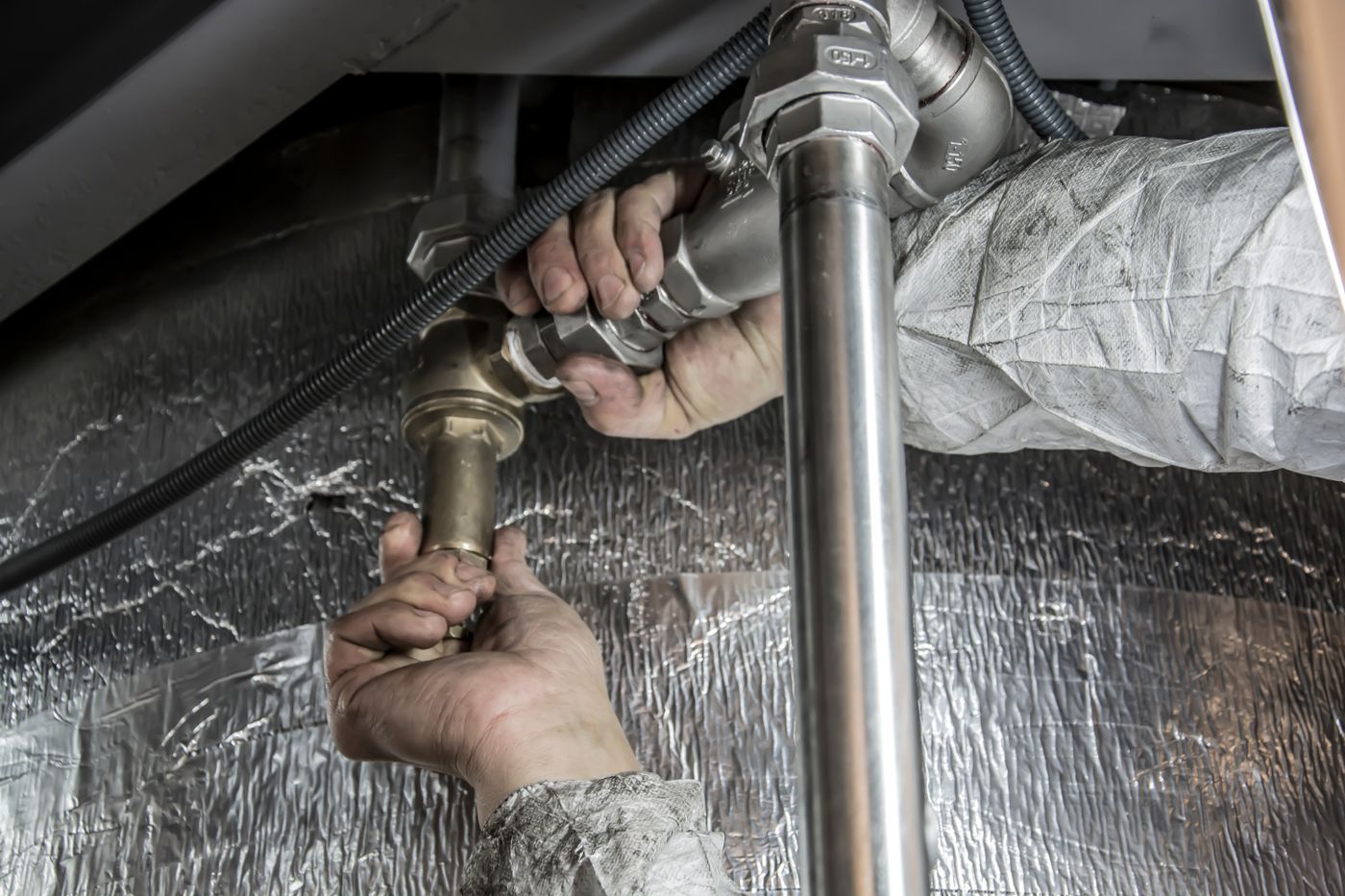 Two hands tightening a brass fitting on a pipe